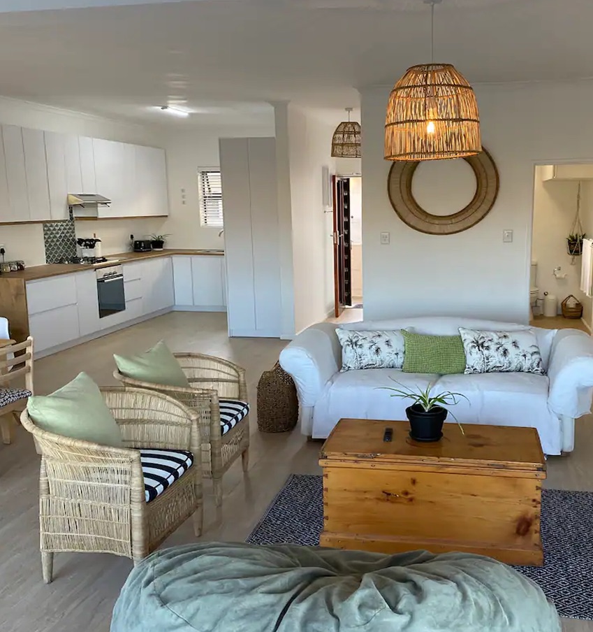 Open-plan living area at Atlantic Apartment, with cane armchairs, a white sofa and a kitchen beyond