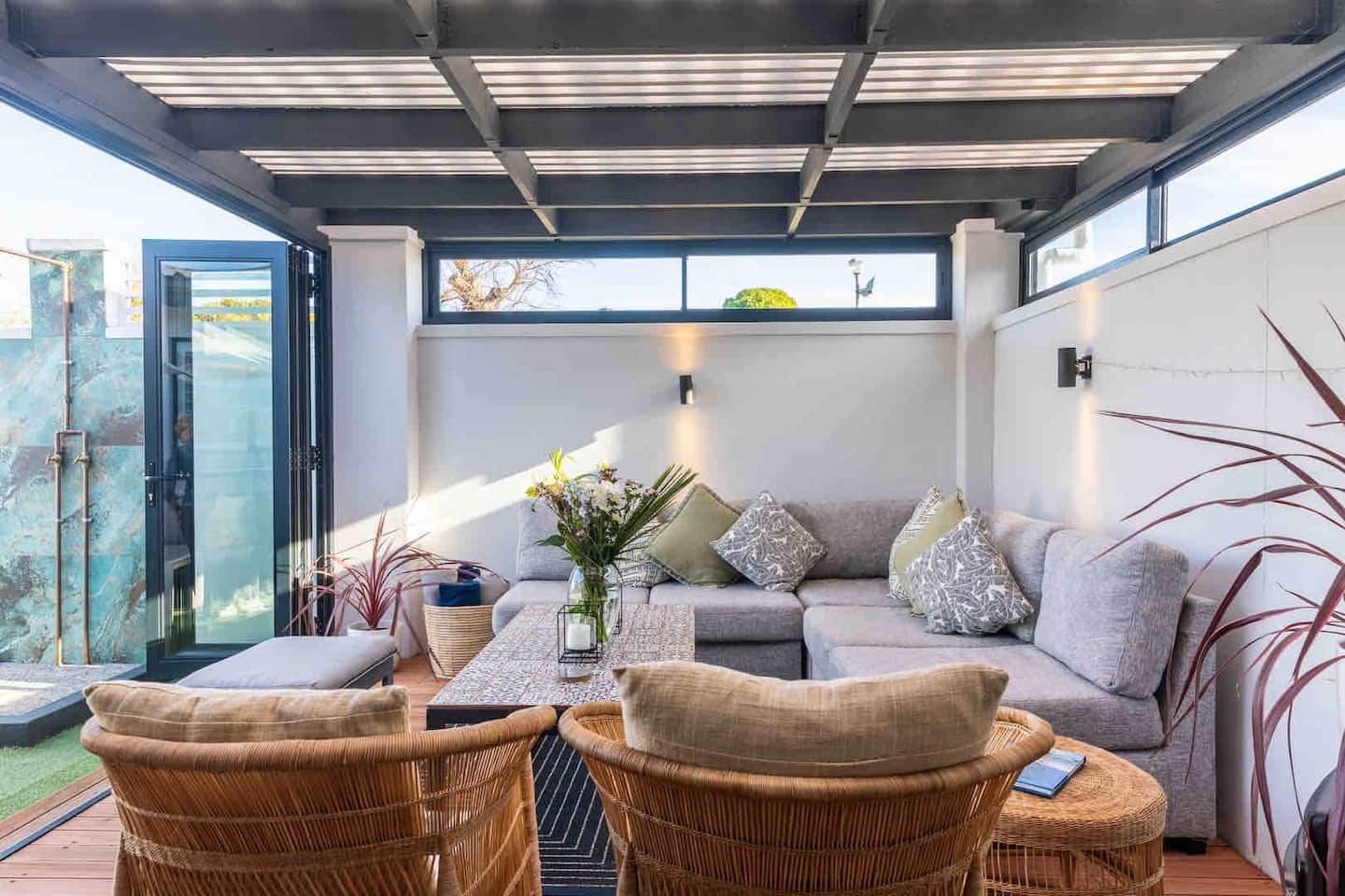 Covered patio lounge at Atlantic Beach Cottage with a grey corner sofa, rattan armchairs and an outdoor shower beyond