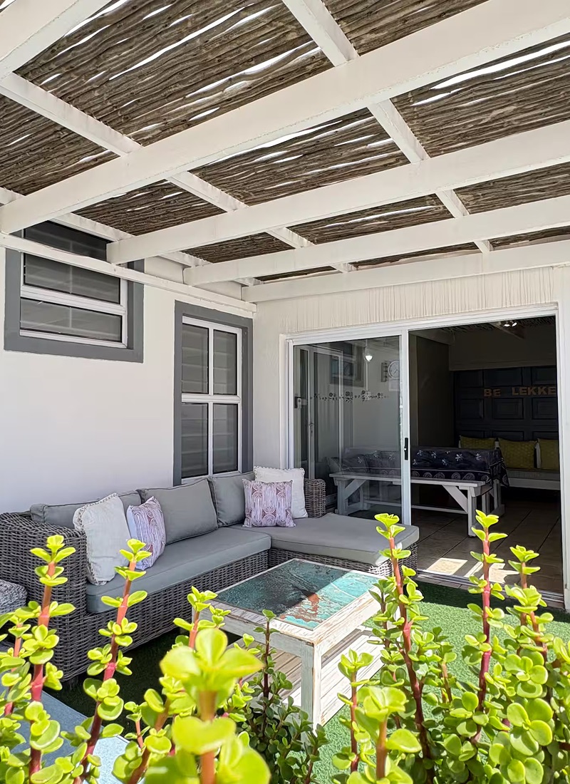Covered patio at Atlantic Crew House, with a corner sofa under a reed-and-beam pergola and sliding doors open to the bunk room