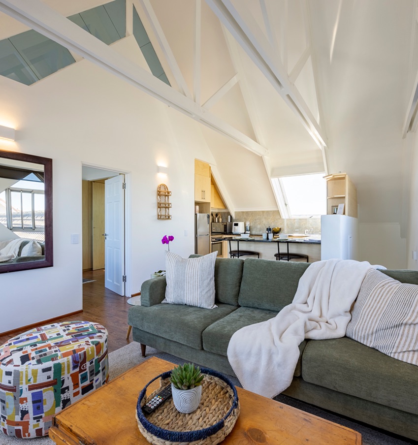 Bright living area at Atlantic Seaview with a vaulted white-beamed ceiling, green sofa and open-plan kitchen